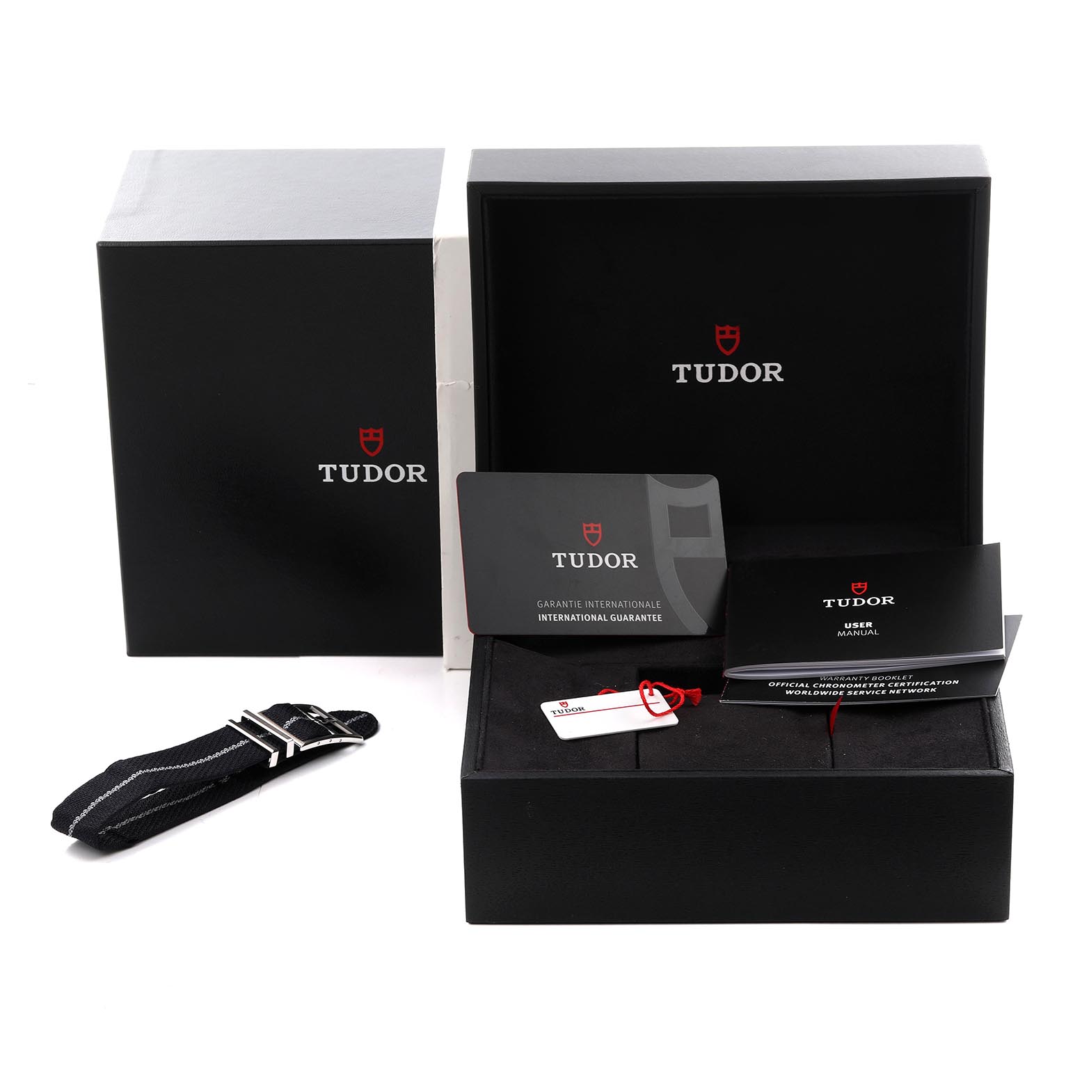 The Tudor Heritage Black Bay 79210 Men
s Ceramic Black Dial 79210 Men
s Ceramic Black Dial watch is shown with its box, guarantee card, user manual, tag, and an extra strap angled from above.